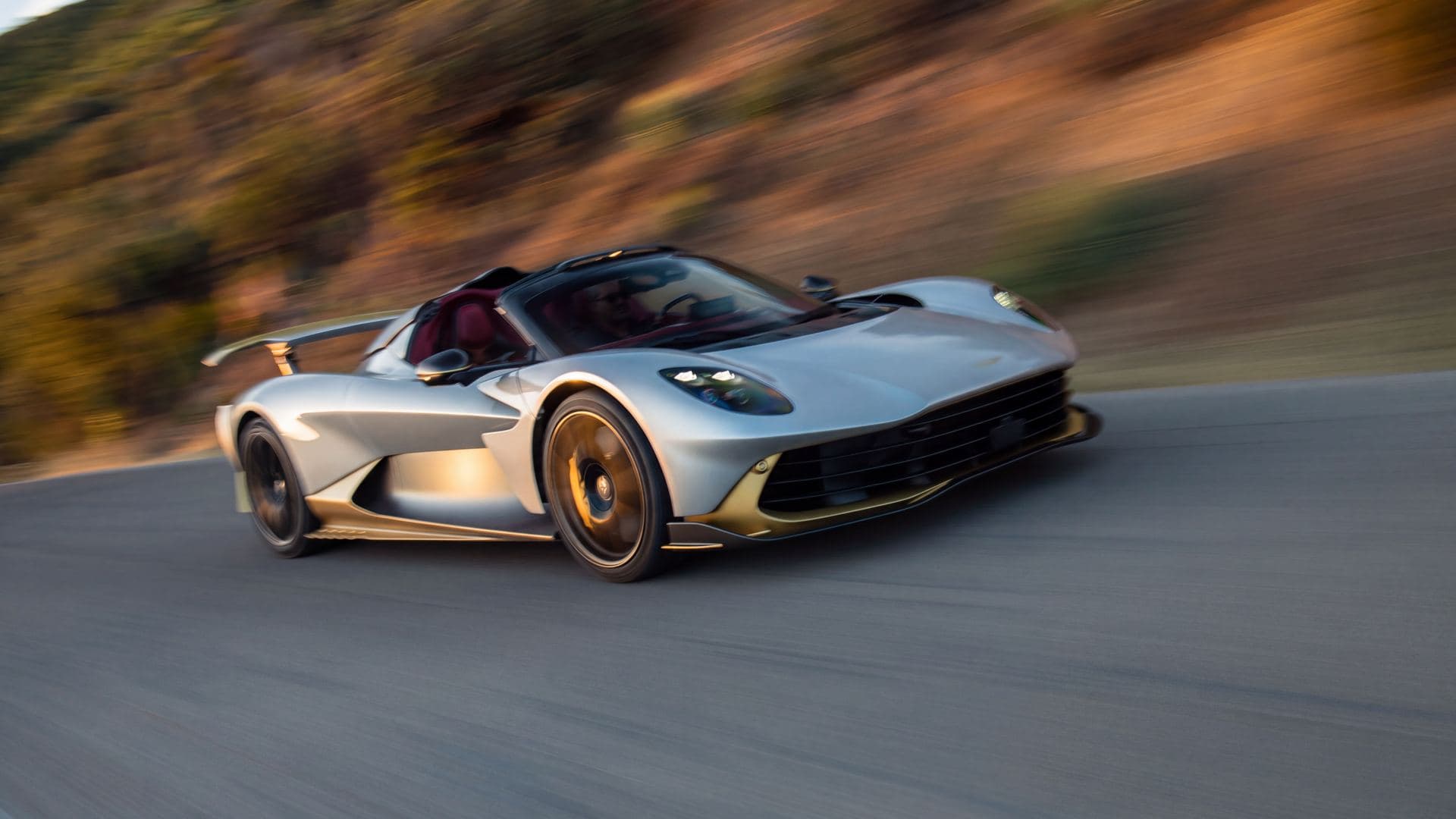 aston martin valhalla spider zilver en goud zonder dak op een heuvelweg