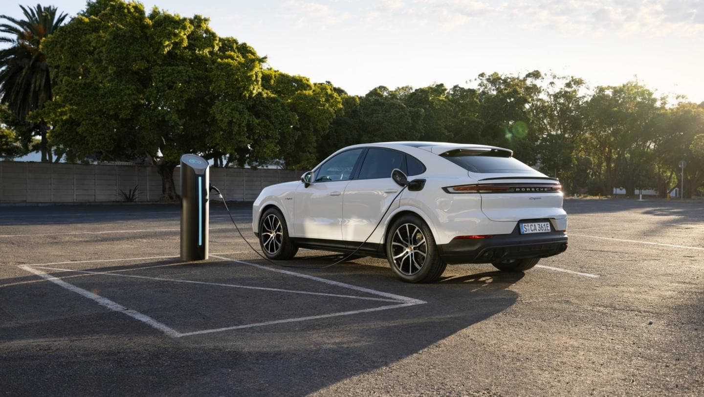 White Porsche Cayenne E-Hybrid Coupé plugged into a charging point in a sunny car park