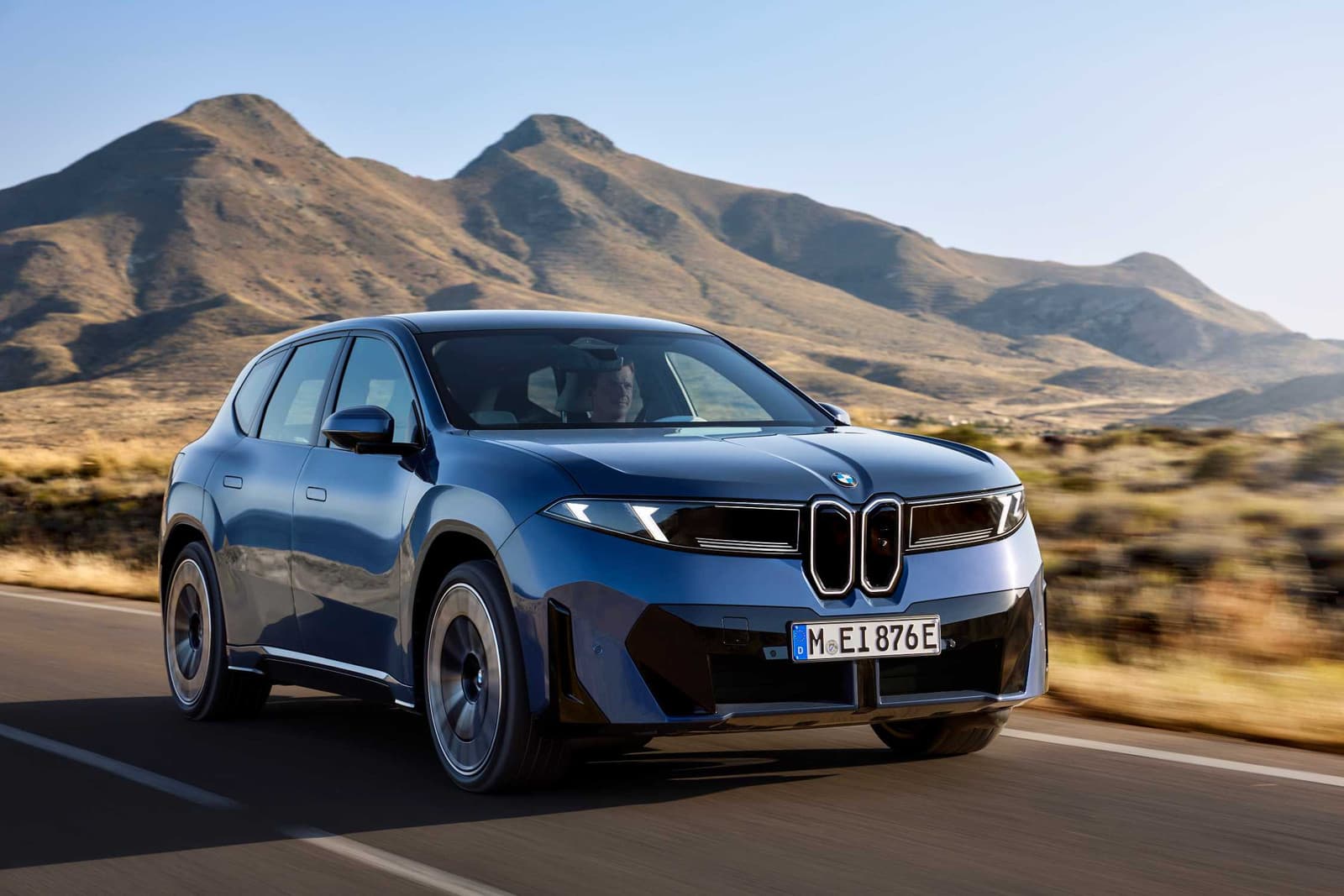 BMW iX3 50 xDrive bleu en mouvement sur une route bordée de montagnes