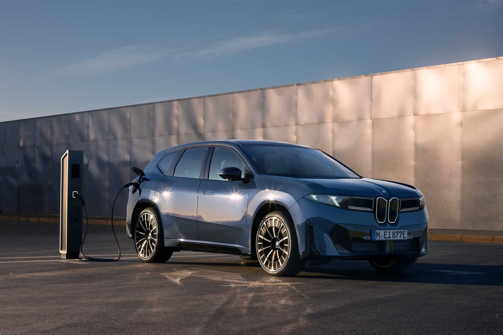 BMW iX3 en charge sur une borne rapide, garé devant un mur métallique